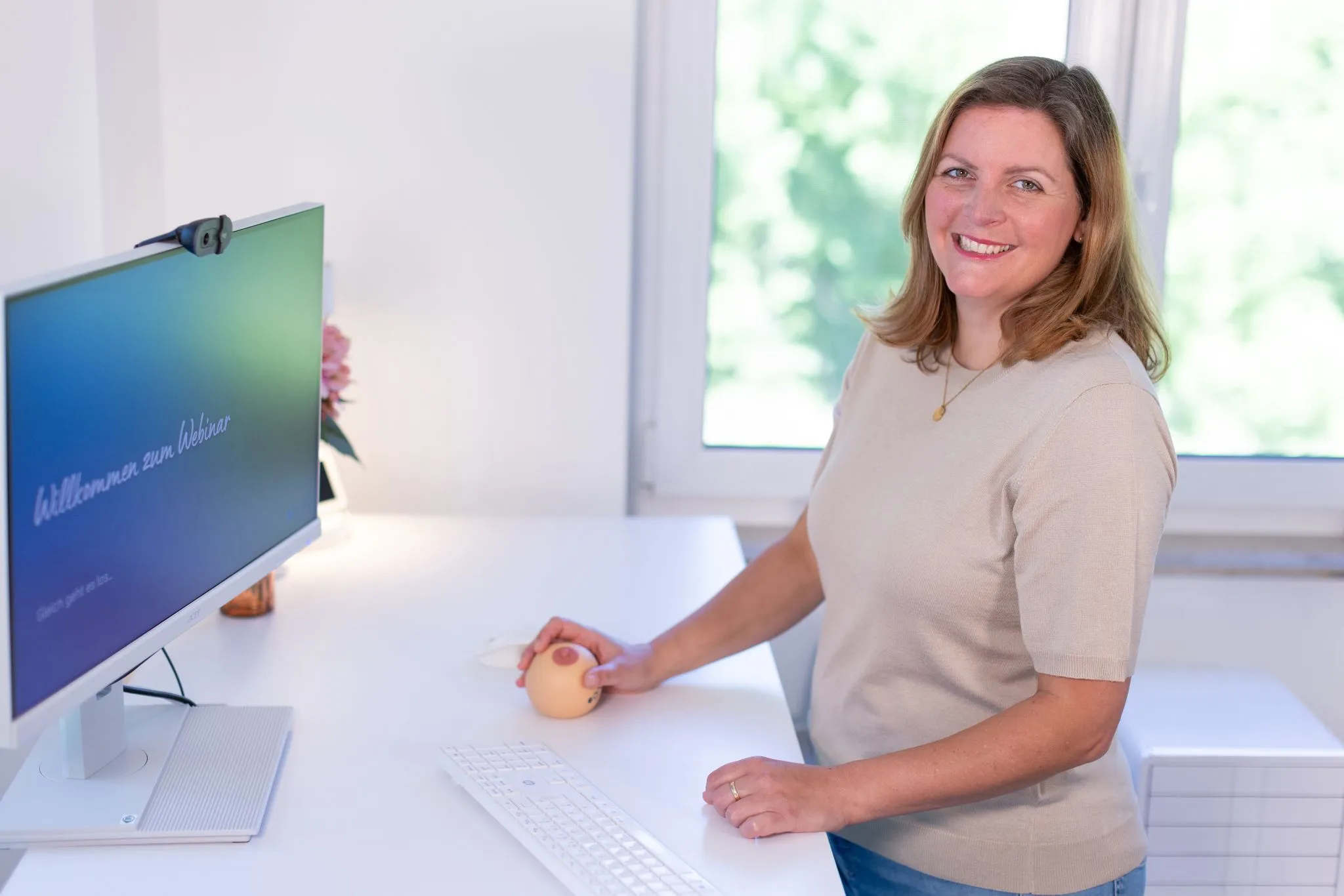 Verena am Schreibtisch mit Brustmodell und Monitor zur Begrüßung eines Webinars